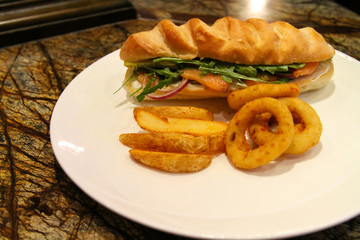 Cold sandwich served with onion rings and fries.