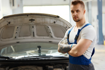 Portrait of a mechanic standing against a car at his workshop