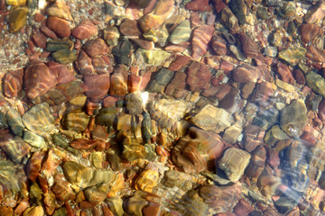 Colored pebbles on the beach with water texture background.
