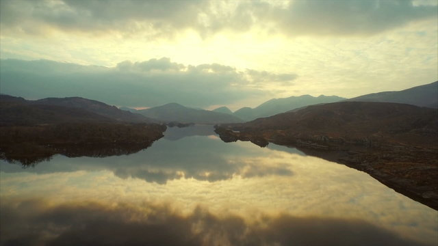 Drone footage of calm reflecting lake and mountains against sky. Tilt up shot of still water with reflection of cloudy sky. Panning shot of mountain range on sunny day. HD 1080 video.