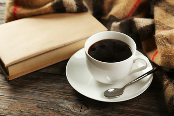 Cup of coffee with plaid and book on grey wooden background