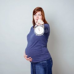 Hochschwangere, erschrockene Frau mit Wecker