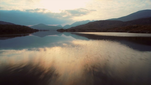 Drone footage of lake and mountains against sky. Fast tracking shot of rippled water and mountain range against cloudy weather. Reflection of clouds is falling in water. HD 1080 video.