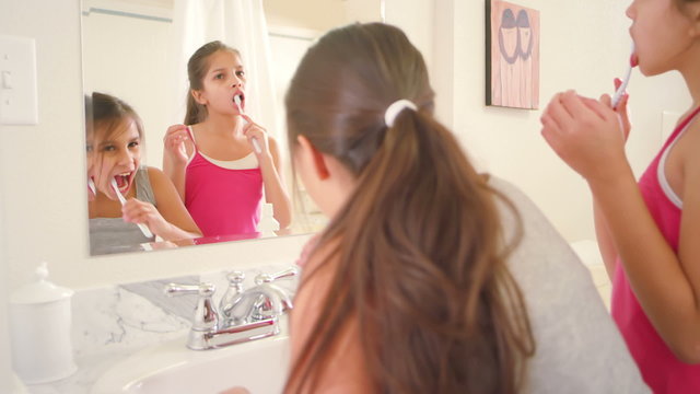 Two adorable little sisters brush their teeth together in the bathroom