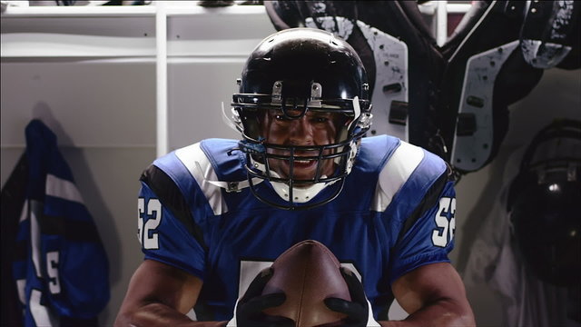 A football player in full pads stands in front of a locker being intimidating 