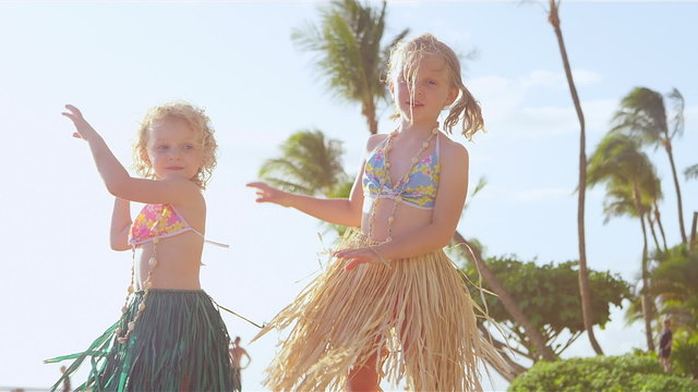 Two young sisters stand and show off their hula dance moves