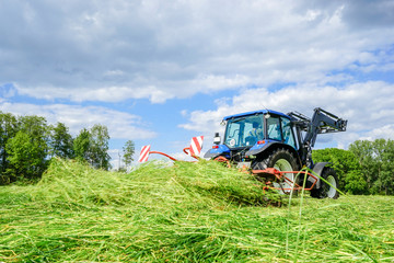 Heuernte, Traktor mit Heumaschine beim Gras wenden