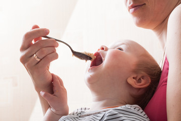 baby feeding spoon of porridge. mouth wide open. maternal care