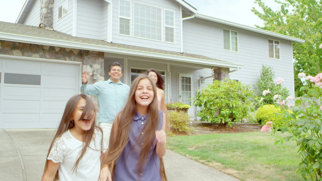 A family runs out of their house towards the camera and then stops and smiles