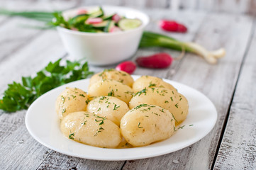 Young boiled potatoes with butter and dill on a white plate