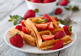 Belgium waffles with strawberries and mint on white plate