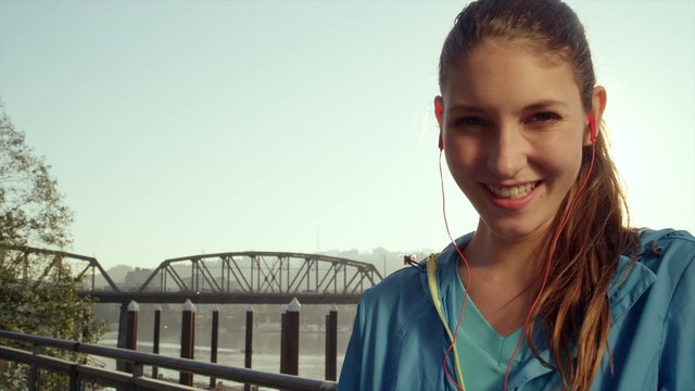 A young woman wearing headphones and running wear, smiles directly into the camera