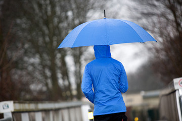 Eine Person in blauer Regenkleidung mit Schirm, unternimmt zum Nachdenken einen Regenspaziergang über eine Brücke 
