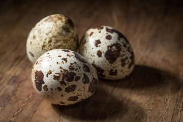 three quail eggs isolated on dark wood table