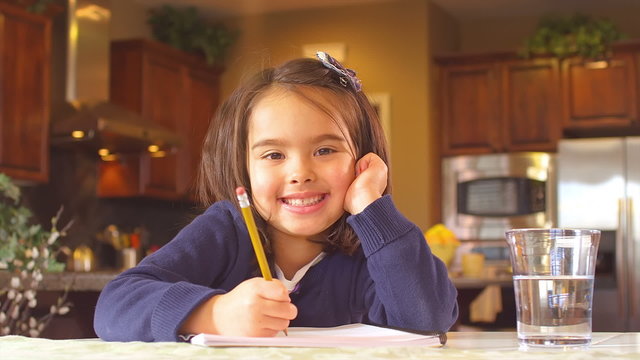 An adorable little girl smiles for the camera as she does her schoolwork