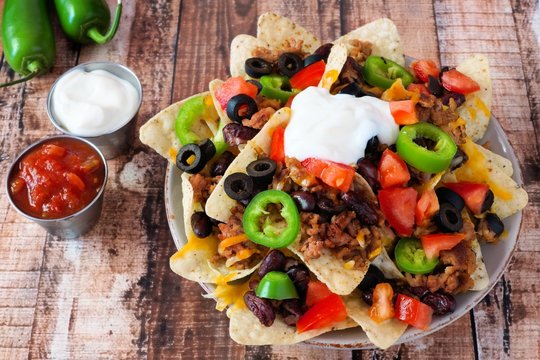 Fully loaded Mexican nachos on rustic wood background