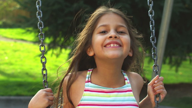 Adorable little girl on a swing smiles for the camera. 