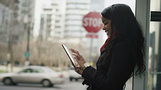 A young woman waits for her bus while playing on her tablet computer