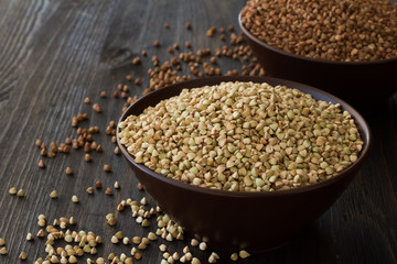 Green and brown buckwheat in ceramic bowls on a wooden surface