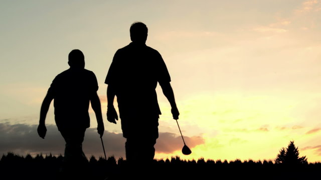 Two older gentlemen walk down a golf course together and talk into the sunset  