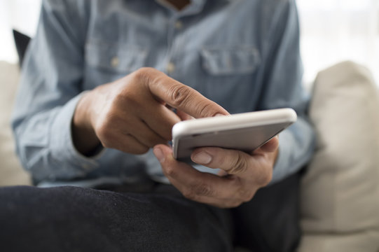 Men are using a mobile phone sitting on the sofa