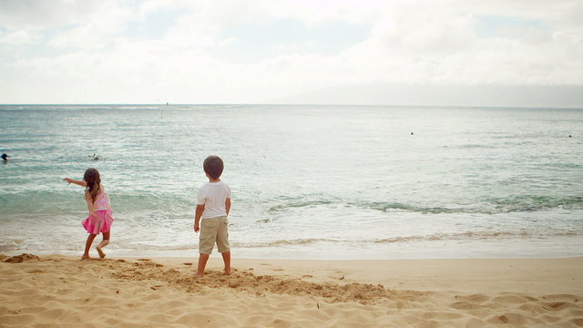 A young boy and girl stand and throw sand into the ocean