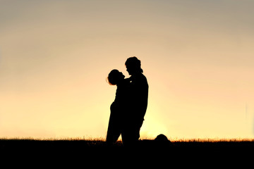 Fototapeta na wymiar Silhouette of Child Laughing and Hugging Father at Sunset