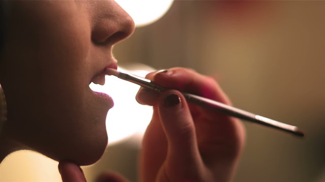 Close up shot of female model getting lipstick applied to her lips by another female
