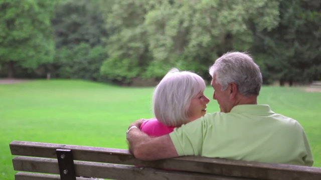 Senior couple sitting on a bench eskimo kiss. Medium shot.