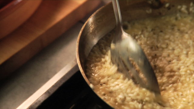 Rice in a pan being stirred with a wooden spoon by a chef to make risotto
