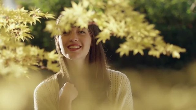 Young woman stands behind leaves and looks into the camera in slow motion
