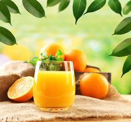 Glass of orange juice on sackcloth on wooden table and natural background