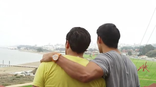 A gay couple stands on a cliff and look out to the ocean