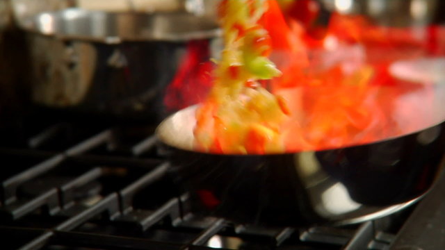 Veggies and oil make fire on a commercial kitchen stovetop grill