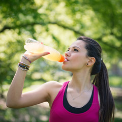 Young woman drinking energy drink outdoors in a park. - 84080119