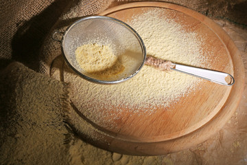 Flour with sieve on wooden cutting board, closeup