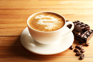 Cup of coffee latte art with grains and chocolate on wooden background