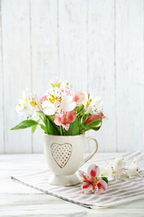 Beautiful flowers in cup, on wooden background