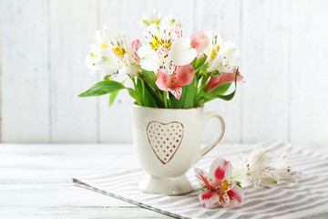 Beautiful flowers in cup, on wooden background