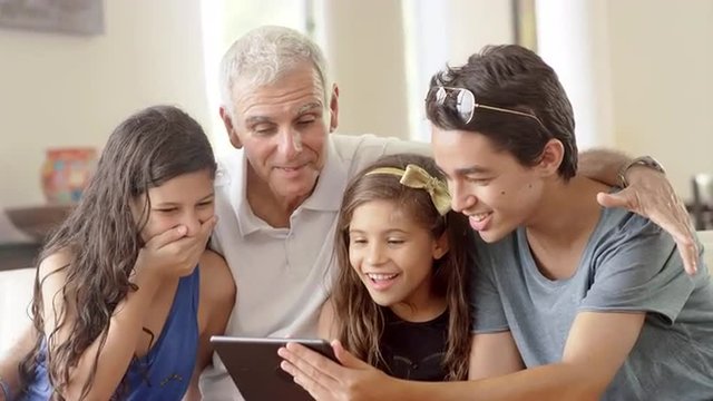 Grandfather using a tablet computer with grandchildren in living room
