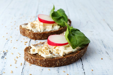 Delicious sandwiches with radish and basil on wooden background