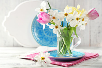 Spring bouquet in glass mug on color wooden background