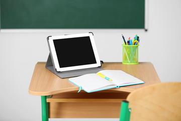Wooden desk with stationery and tablet in class 