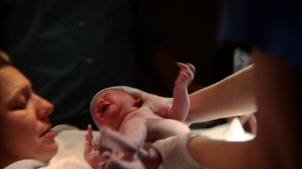 Newborn baby being held up and handed to its mother.