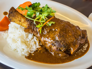 Spicy lamb shank rendang served with rice and vegetables
