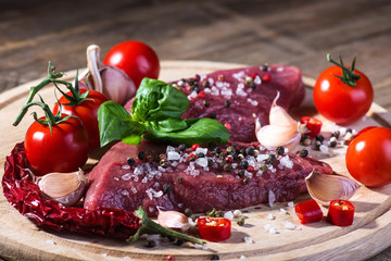 Raw beef steak with spices on a wooden background