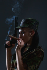 Female soldier in camouflage uniform with gun and cigar smoke