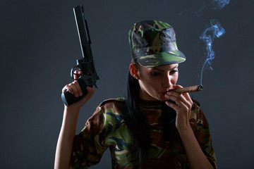Female soldier in camouflage uniform with gun and cigar smoke