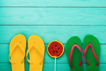 Colorful summer accessories and watermelon candy on blue wooden background.