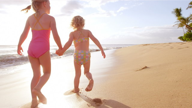 Two adorable little girls hold hands and walk down a beautiful beach together